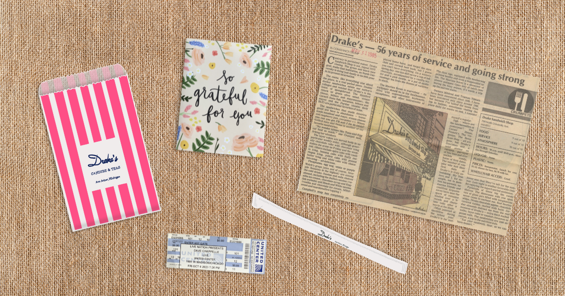 A flat lay of keepsakes on a burlap surface, including a pink striped bag, a gratitude card, a vintage newspaper clipping, and a worn straw — small things kept for the feelings they hold.
